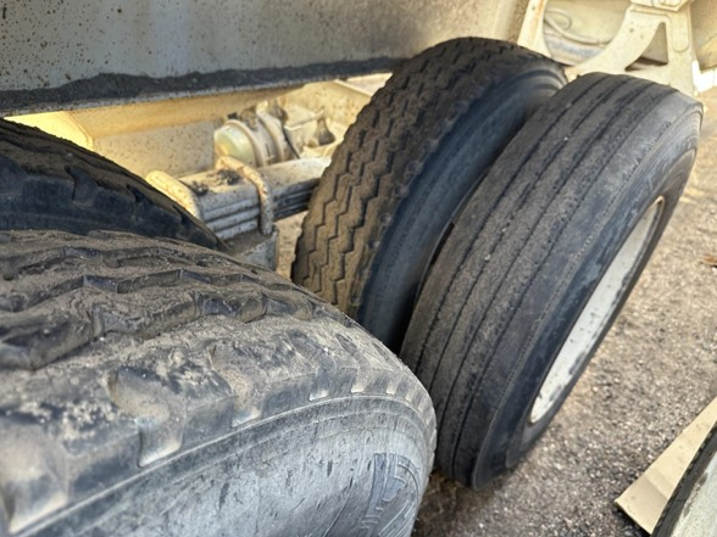 Trailer dual axle wheels and suspension undercarriage with tires and mud, showing steel frame and leaf spring components.
