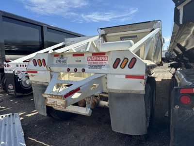 Trailer rear view of a 2015 unknown spring ride steel bottom dump with warning label and dual axles, white paint, and metal mud flaps.