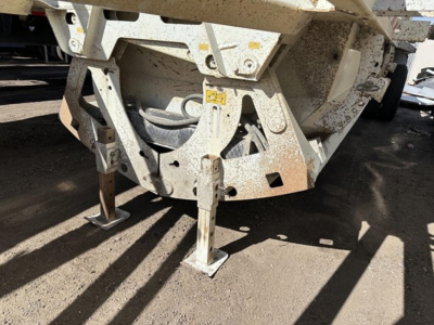 Dump trailer hitch area with steel bottom dump frame and support legs, showing undercarriage and muddy components.