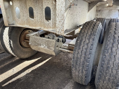 Trailer undercarriage showing dual rear axles with heavy steel frame and leaf spring suspension; rusted components; tires visible.