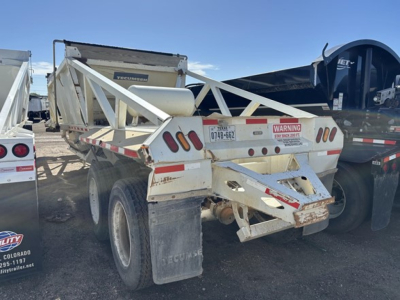 Dump trailer showing white steel bottom dump with triangular frame, rear angle and taillights. Visible branding: TEKURRO? and warning sticker, license plate, dual rear tires, mud flaps.