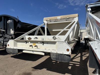 Dump trailer with steel bottom bed in view showing triangular truss sides and rear bumper with reflective lights.