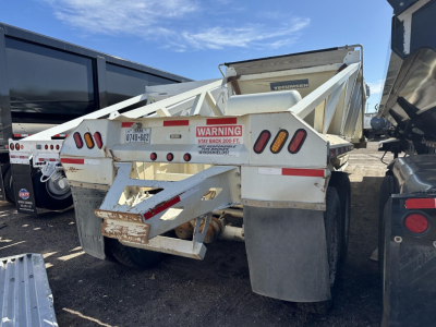 Dump trailer showing dual axle steel bottom dump with warning label and rear pins.