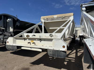 Dump trailer showing steel bottom and electric flip tarp support in a yard; front bumper, side rails, and rear drop area visible.