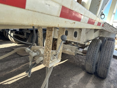 Trailer undercarriage showing hitch assembly, hydraulic lines, and dual rear wheels of a steel bottom dump trailer.