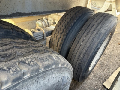 Trailer dual axle wheels and suspension undercarriage with tires and mud, showing steel frame and leaf spring components.