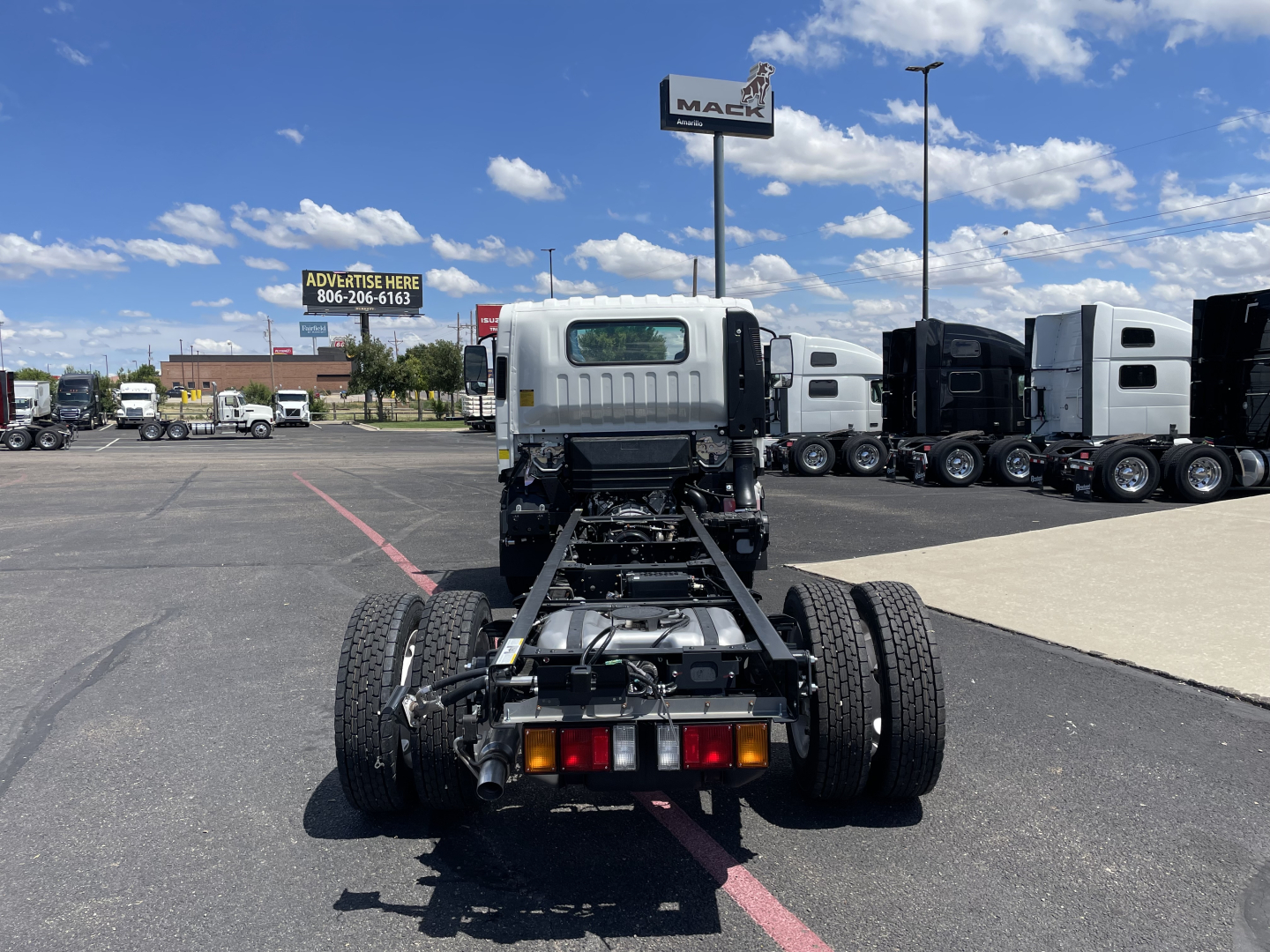 Isuzu NRR cab and chassis rear view showing chassis frame, dual rear axles, and rear lighting; clean lot with trucks in background.