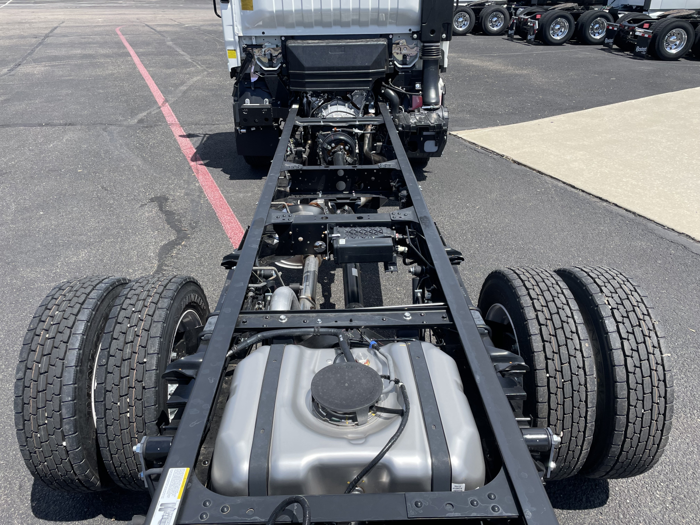 Isuzu NRR cab and chassis frame showing fuel tank and dual rear axles with chassis rails and cab in background.