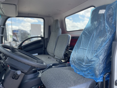 Isuzu NRR cab interior view showing driver seat and blue plastic-covered passenger seat.