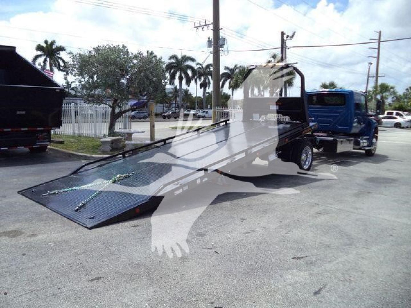 Wheel-lift rollback tow truck on a trailer, with loading ramp extended; no legible manufacturer text visible on the image.