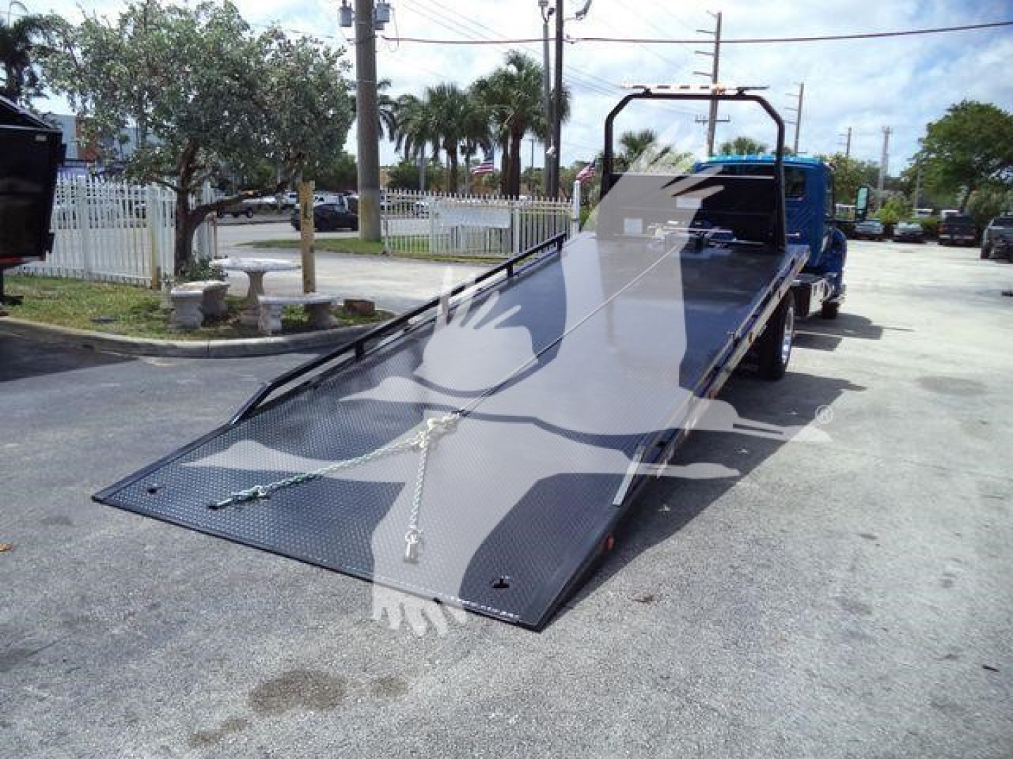 Truck bed tow rollback flatbed with large ramp on a blue truck, loading ramp lowered, metal checker-plate surface and safety chains visible.
