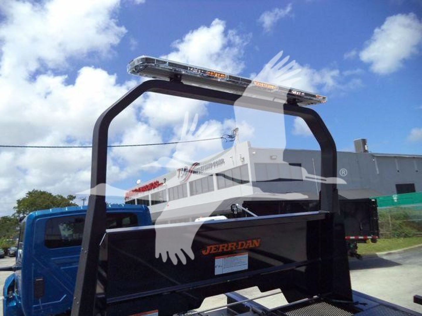 Truck bed with Jerr-Dan rollback equipment mounted, light bar on top, International MV equipment in the background.