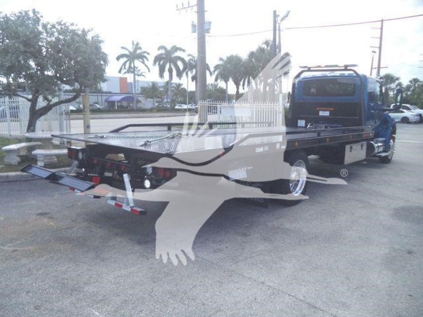 Truck bed rollback tow truck with flatbed and hitch, blue cab, rear view showing loading equipment.