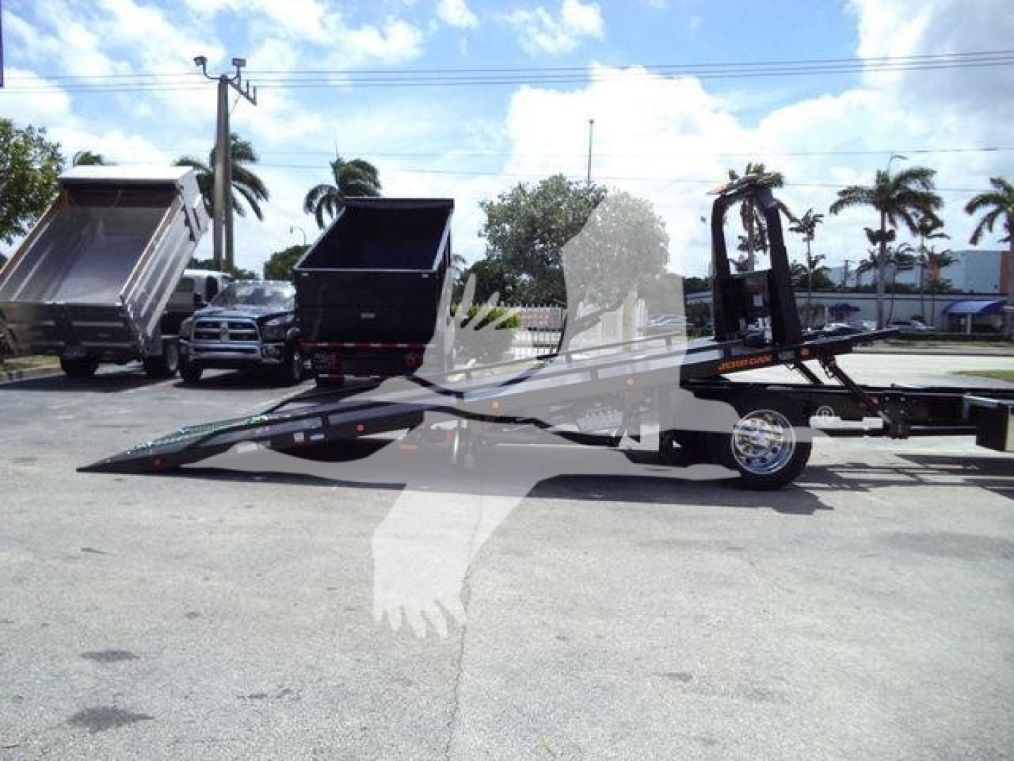 Truck rollback trailer on a lot with a dip bed and hydraulic ramps, International MV logo may be present; foreground shows a flatbed with a raised gooseneck and tilt bed design.