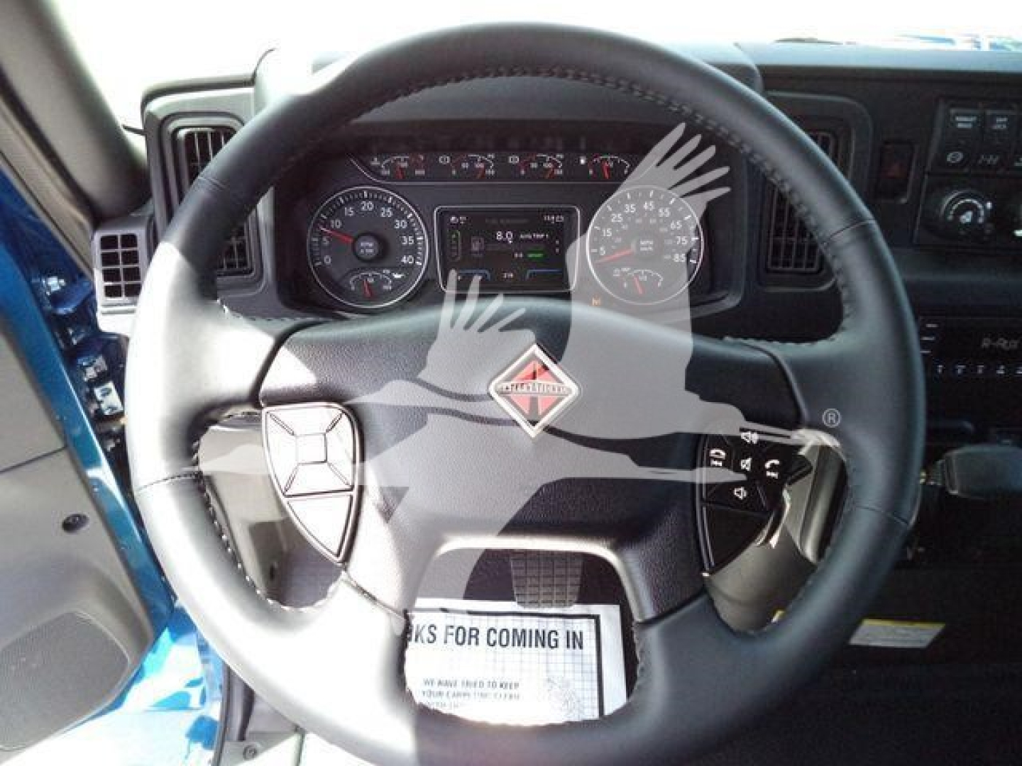 Interior view of a new International MV truck steering wheel and dashboard showing instrument cluster, gauge dials, and controls.