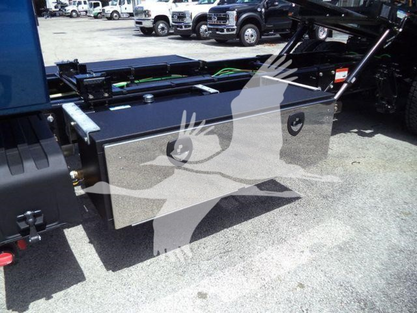 Toolbox mounted in truck bed with hydraulic rollback equipment visible, reflective metal storage box and cables nearby.