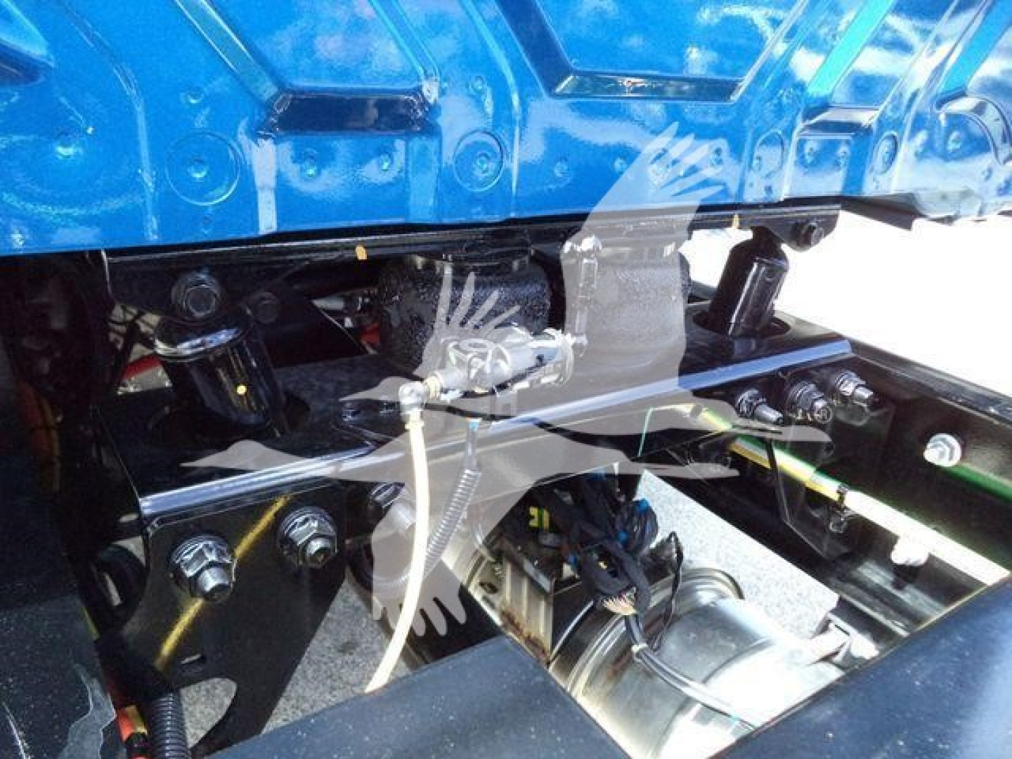 Truck chassis and hydraulic lines visible under blue International MV cab showing wiring harness, hoses, and mechanical linkages.