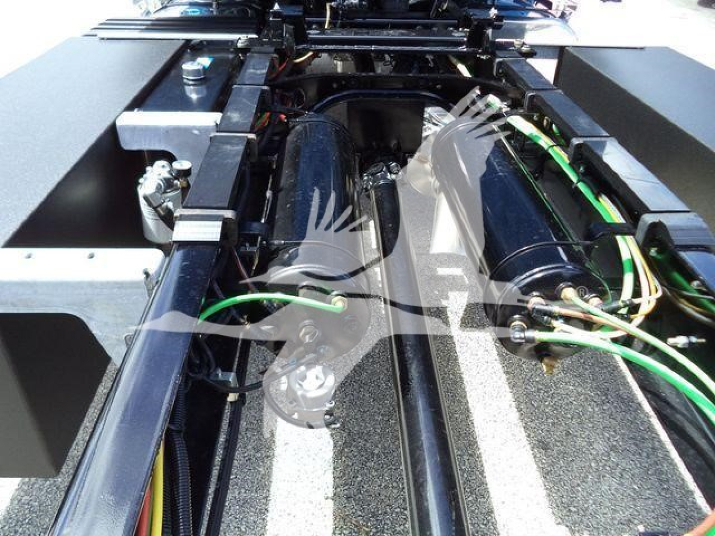 Truck chassis underside showing hydraulic lines and frame rails with green hoses and electrical cables.