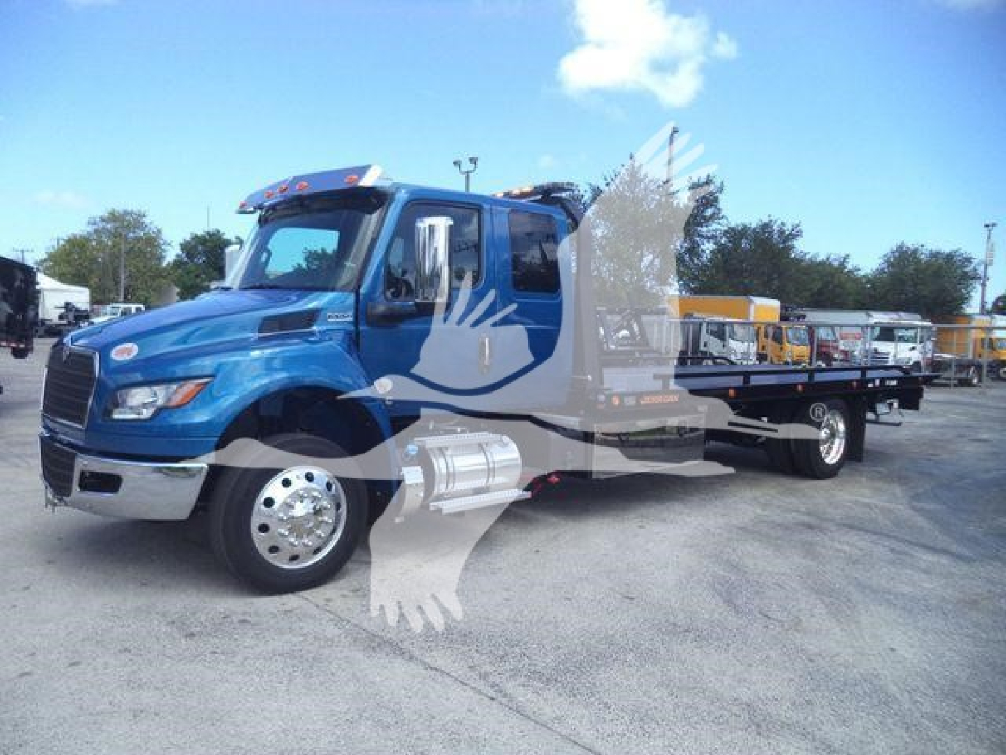 Blue 2027 International MV rollback truck with a long flatbed and chrome fuel tanks. Visible lettering on side includes International logo and cargo area. Showroom or dealership lot in background.