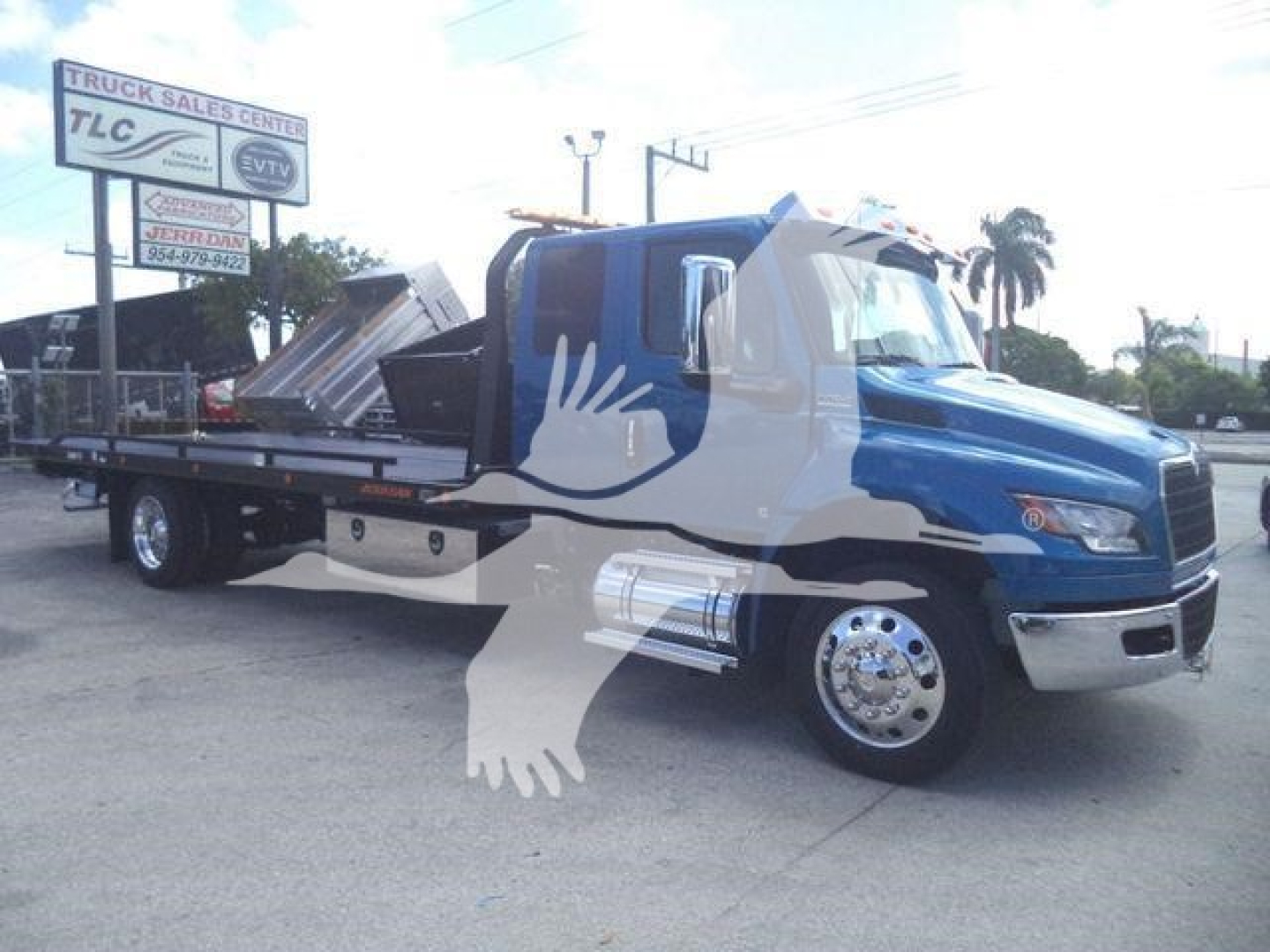 Blue and white International MV rollback truck in showroom lot shown from front-left side with flatbed and crane arm.