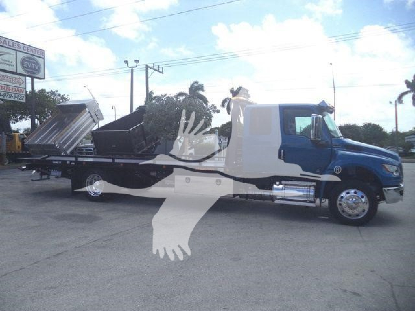 Blue and white International MV rollback truck visible in side view showing cargo bed and hydraulic components.