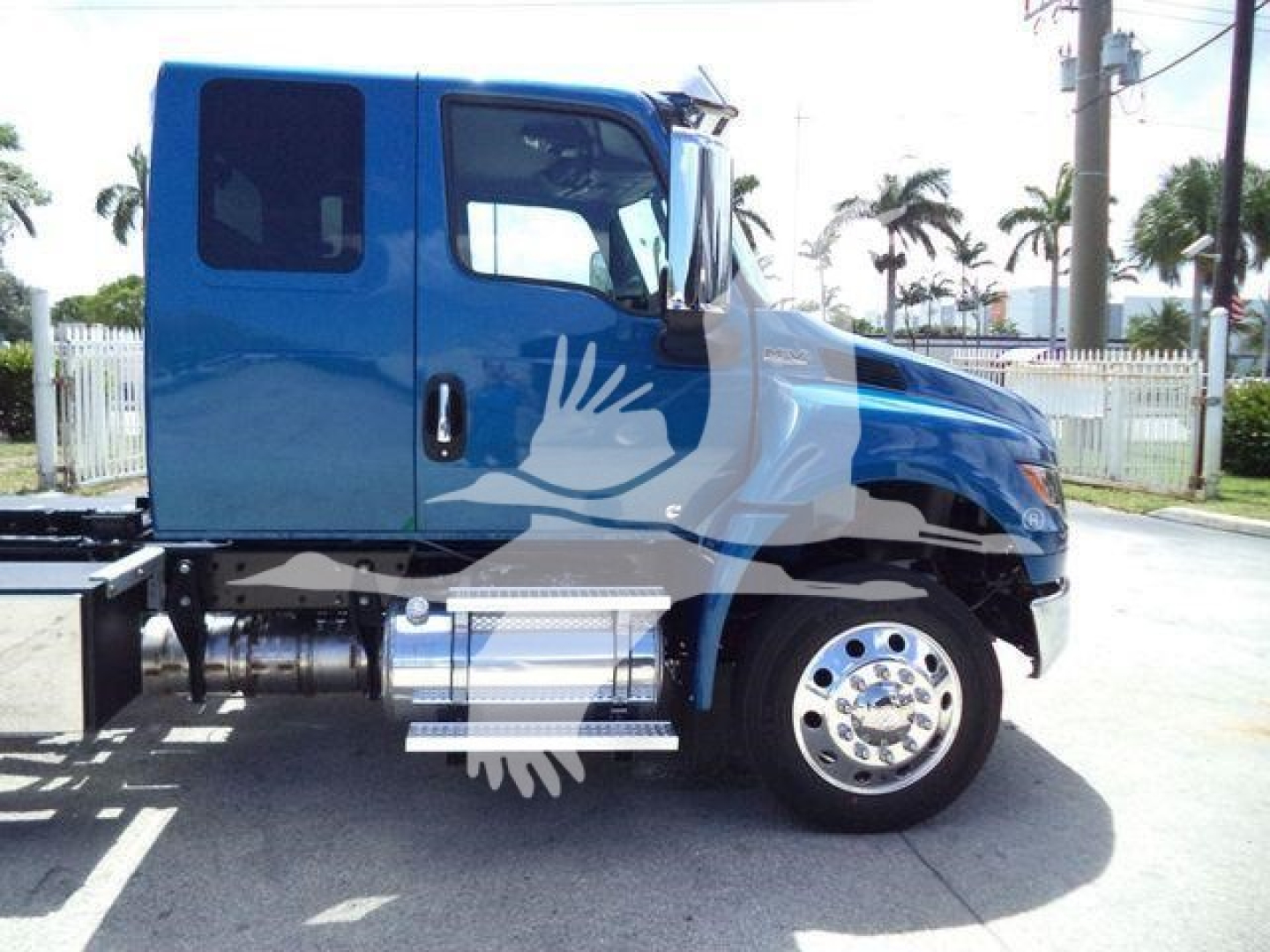 Truck cab side showing blue International MV with chrome fuel tank and steps; no visible text legible on image.