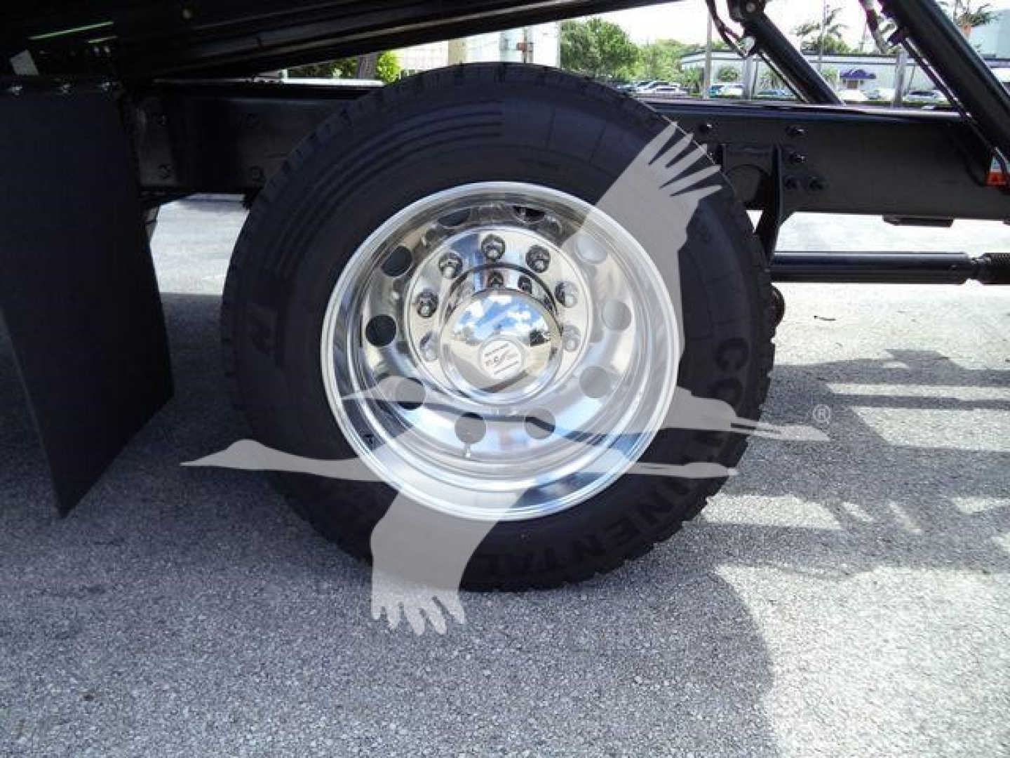 Truck wheel and undercarriage view showing a polished chrome wheel with black tire; overlay watermark with a faint hand and ribbon across the image.