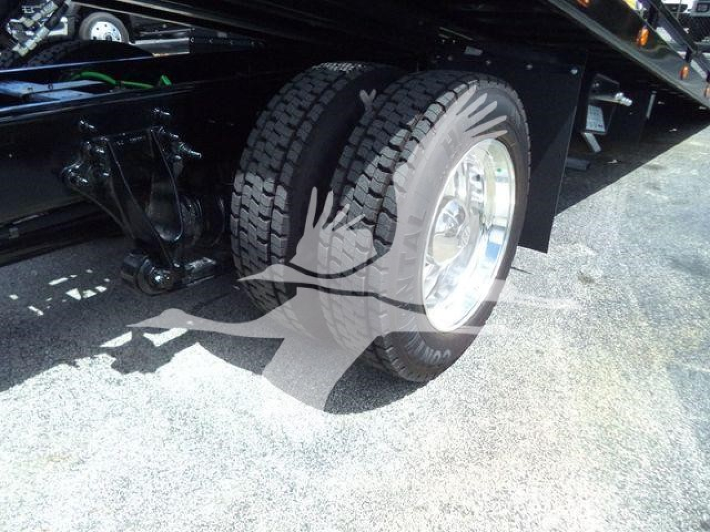 Truck wheel and suspension undercarriage showing heavy-duty tire on a rollback chassis with reflection overlay.