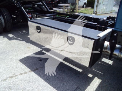Truck tool storage box mounted under a heavy-duty rollback truck chassis; reflective chrome finish with two circular handles; visible side rails and frame.