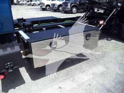 Toolbox mounted in truck bed with hydraulic rollback equipment visible, reflective metal storage box and cables nearby.
