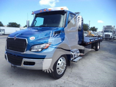 Truck showing International MV rollback truck with blue and white cab in a dealership lot.