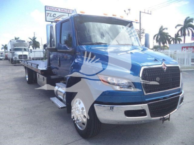 Truck showing blue International MV rollback flatbed with chrome bumper and grille, side mirrors, and large front fender; palm trees in background.