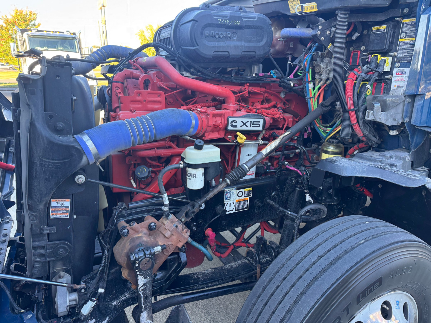 Kenworth T680 engine bay showing ExiS 15 engine and red intake manifold with blue intercooler hose, radiator, and various wiring.