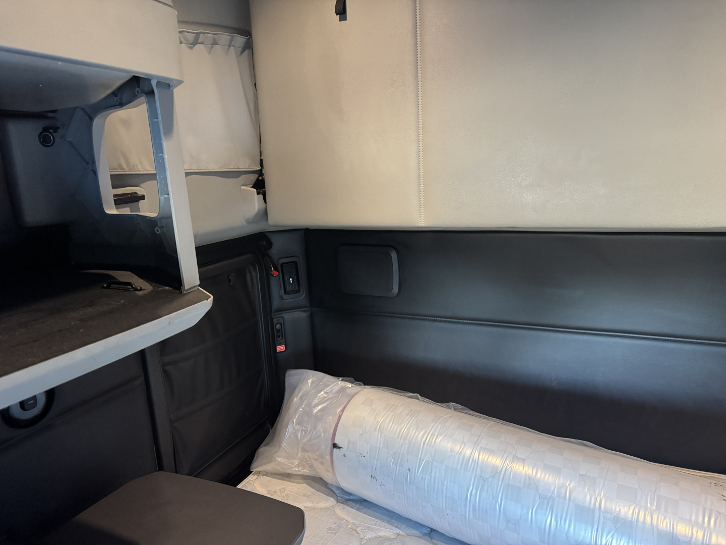 Kenworth T680 truck interior showing sleeper cab area with storage shelf and rolled ductwork in bed area.