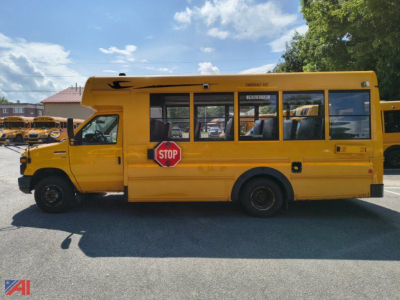 Side view of a yellow Ford E-Series school bus with stop sign, black windows, and seating visible through windows.