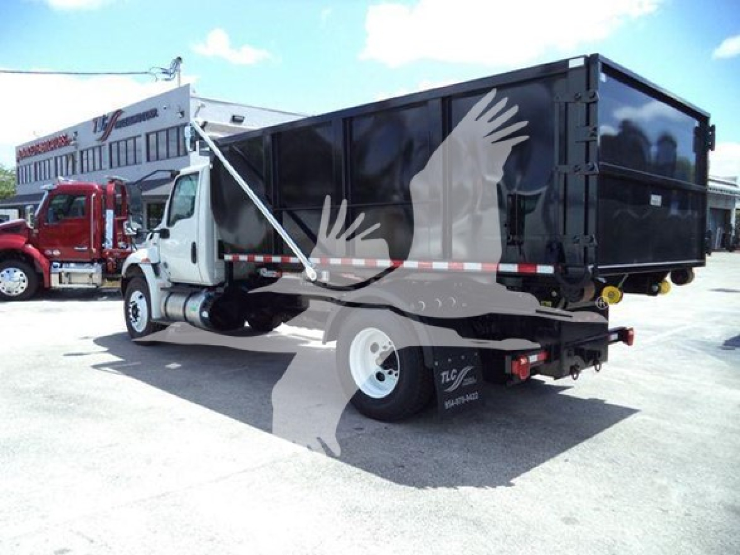 Truck side/rear view of a 2019 International Durastar 4300 roll-off truck with black dump container, white cab, and stock number T22676 plate on a dealership lot.
