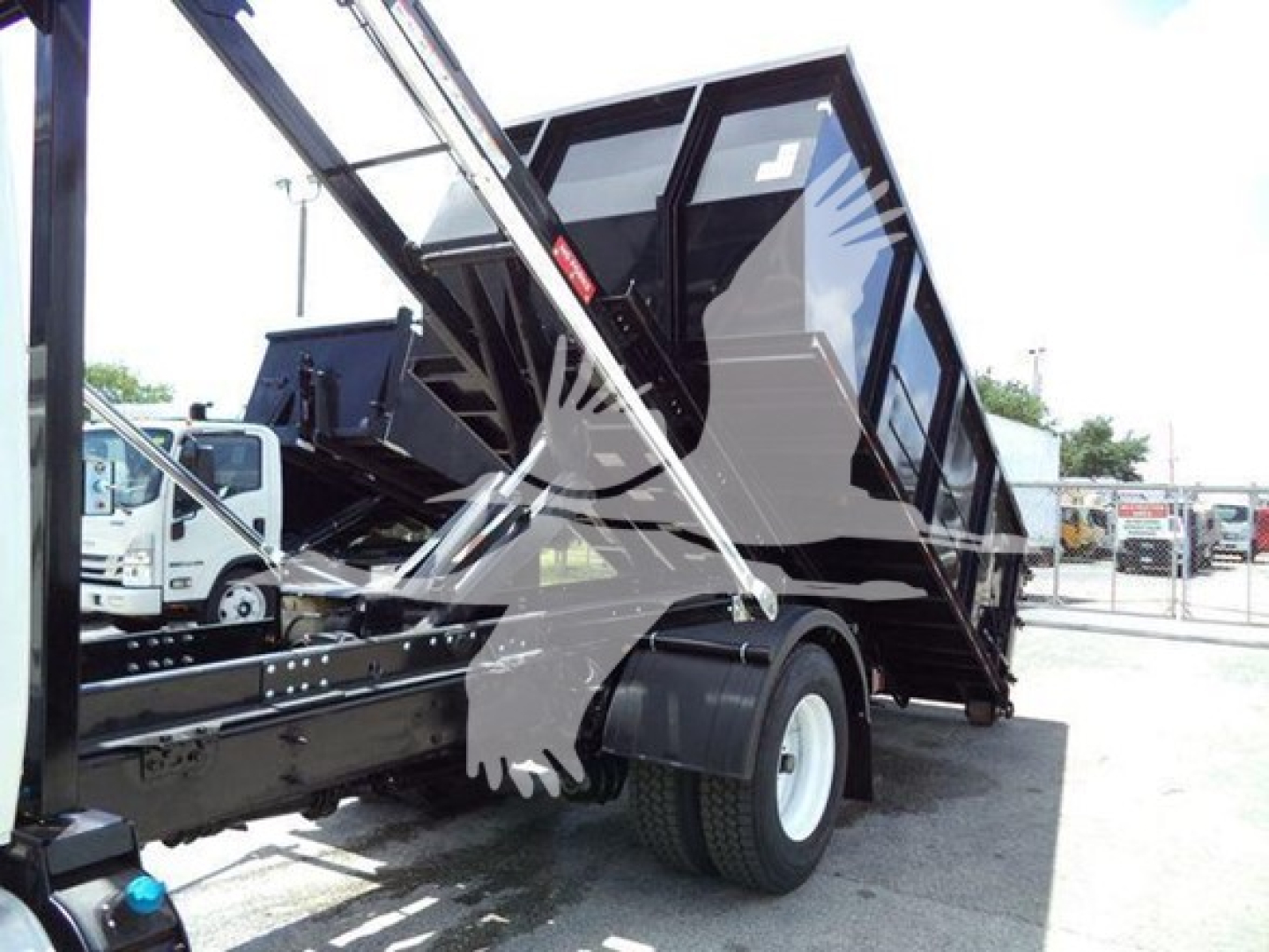 Truck bed with a raised black dumping container mounted on a chassis, with hydraulic arms and a tilted bed for dumping.