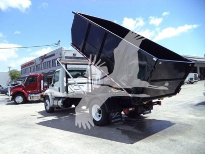 Dump truck in-service showing dump bed raised on 2019 International Durastar 4300 with roll-off body and rear loader in an outdoor lot.