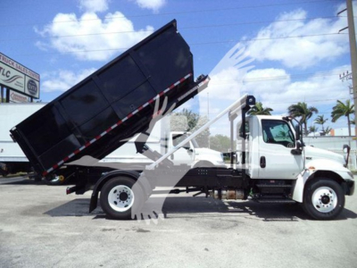 Truck in profile view showing dumping bed raised on a white 2019 International Durastar 4300 roll-off truck.
