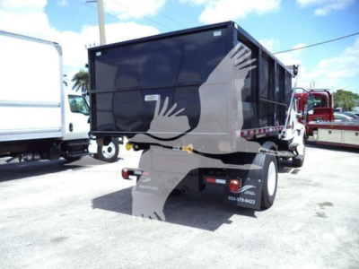 Dump truck/roll-off truck rear view with black container and dual rear lights; visible text includes contact numbers on fender and tail area.