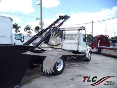 International Durastar 4300 roll-off truck with hydraulic loading arms visible; side shows white cab, black bed, and a bit of a red truck in background; no legible model text or stickers visible.