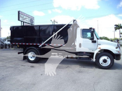 Truck side view showing a white International Durastar 4300 roll-off truck with a black dump body.