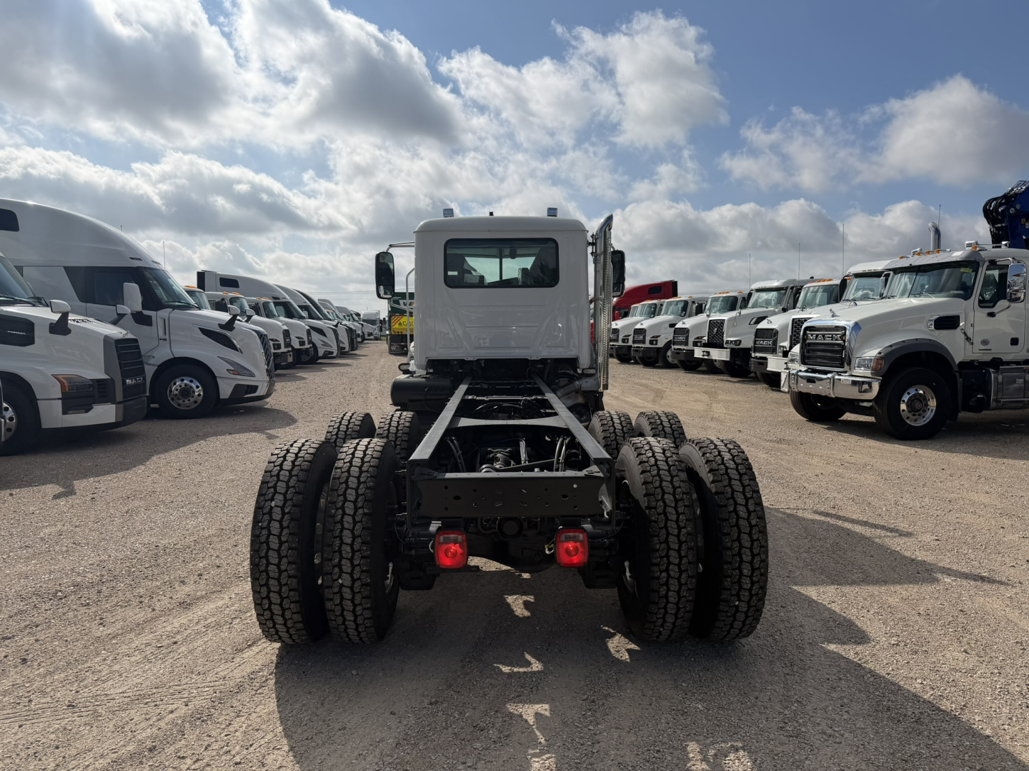 Rear view of a 2026 Mack GR64F cab and chassis showing dual rear axles with dual wheels and a white cab, in a dealership lot with other trucks; no visible text on the image besides the vehicle itself.