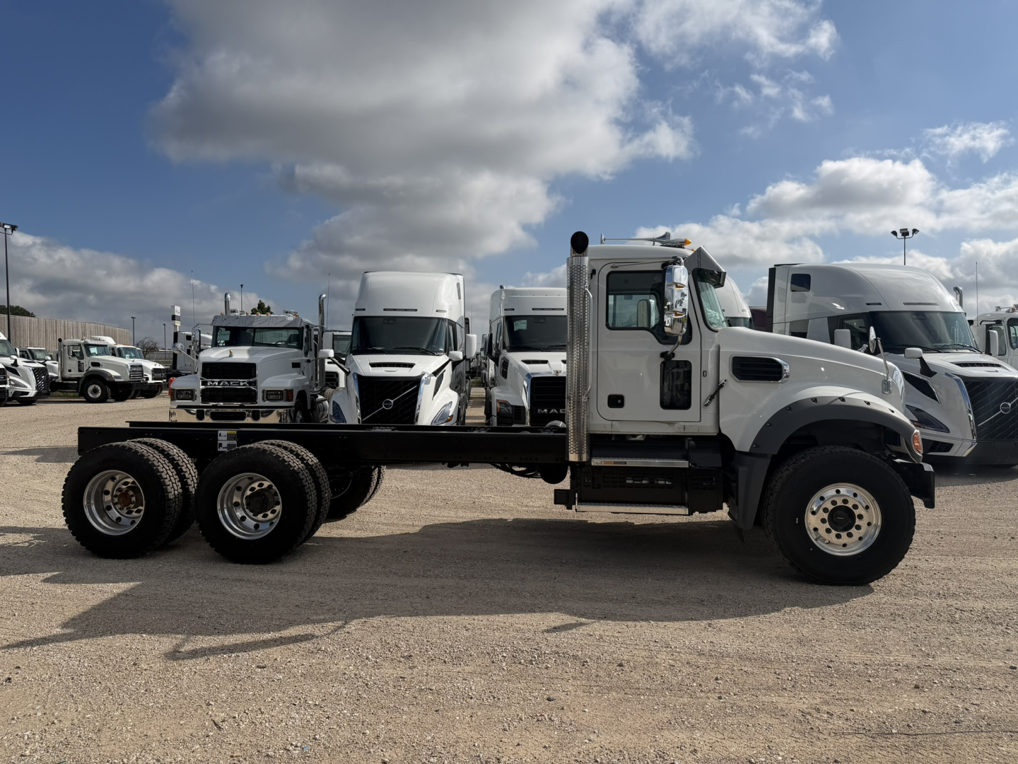 Truck chassis showing 3-axle Mack GR64F cab and chassis with empty bed and white cab.