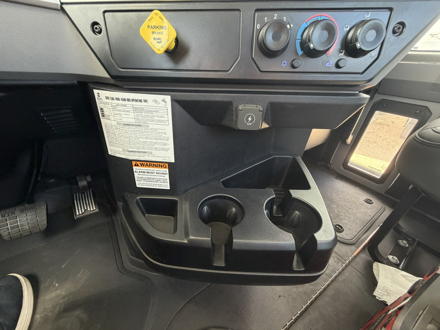 Mack GR64F cab interior showing control panel, ignition and dashboard, cup holders, and yellow engine stop/air switch label.