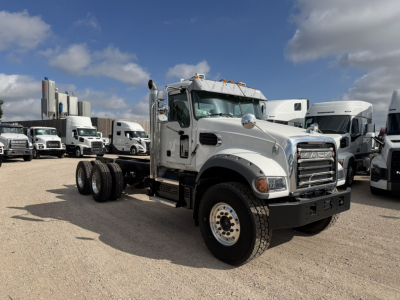 Mack GR64F cab and chassis truck in a lot showing front grille, dual rear axles, and surrounding trucks.