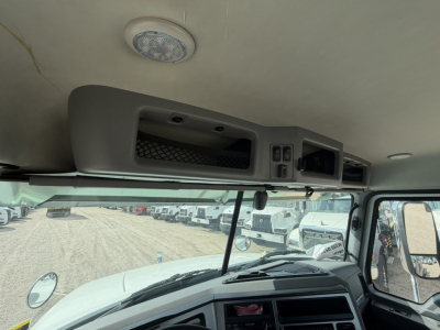 Mack GR64F cab interior view showing overhead storage compartments and dashboard controls, forward windshield with side mirrors, and interior roof panel.