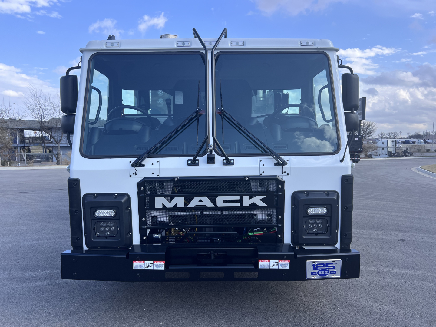 Mack LR64 daytime view showing front cab with large 'MACk' grille, dual windshield wipers, and bumper with stickers.
