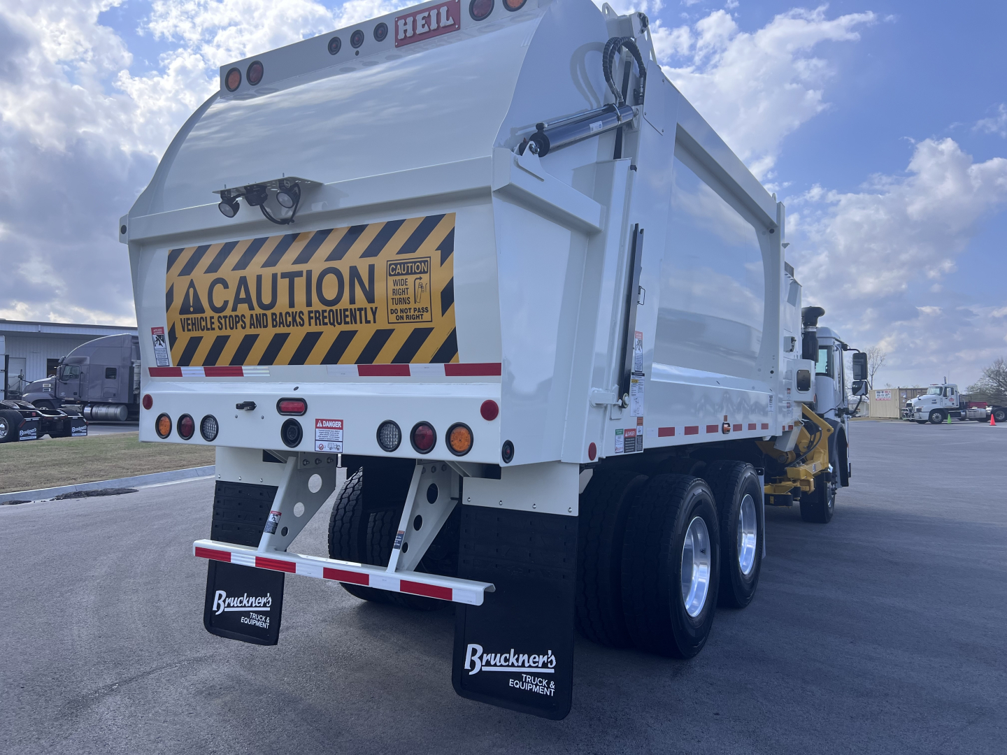 Rear view of a 2026 Mack LR64 dump/truck showing caution signage and taillights.