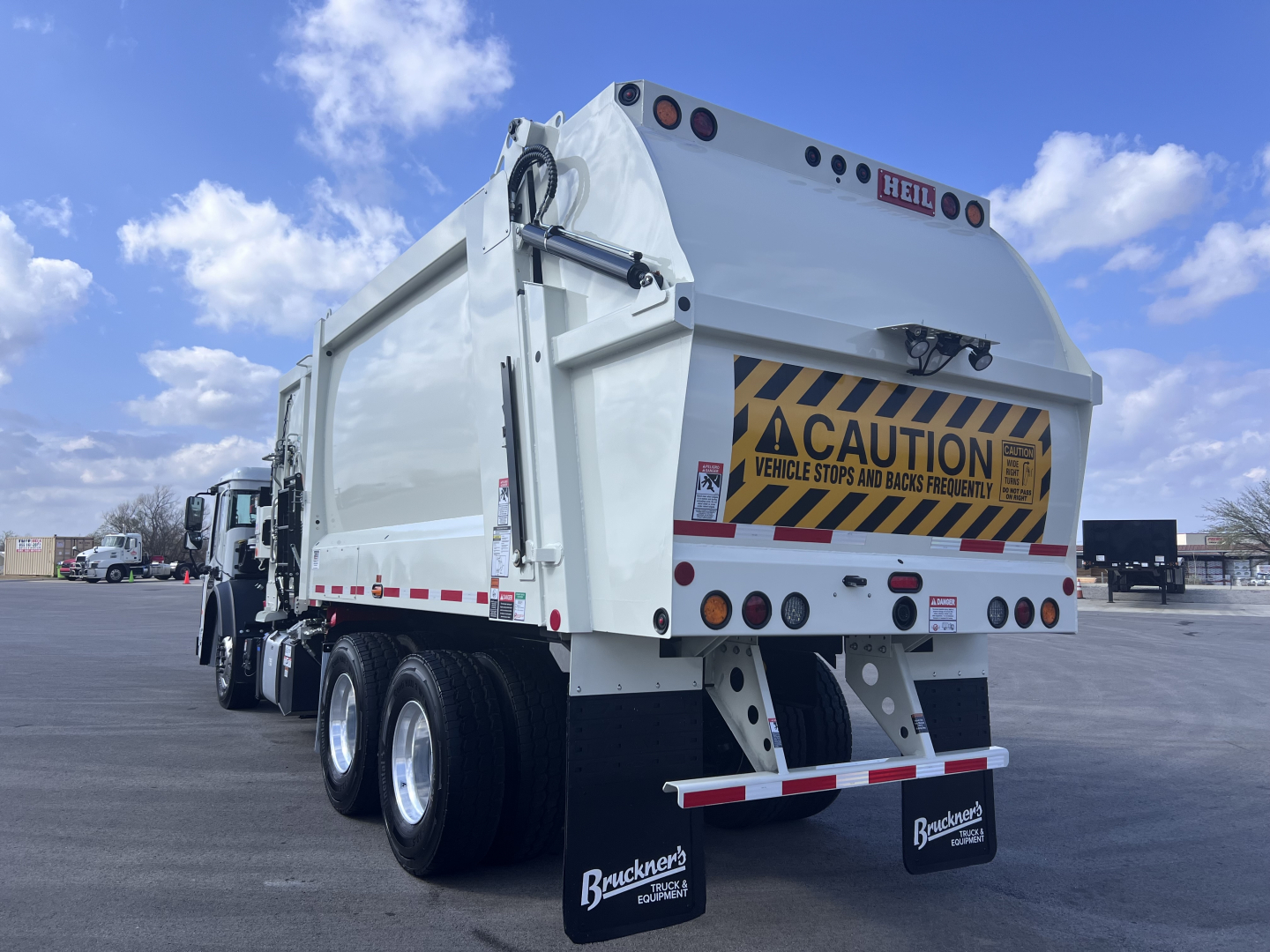 Rear view of a white Mack LR64 dump truck showing cargo box and taillights with caution sign and license plate area.